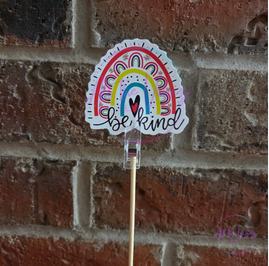 Be Kind rainbow vinyl sticker displayed on a clear clip against a brick background. Sticker for water bottles, laptops, tumblers, and notebooks.