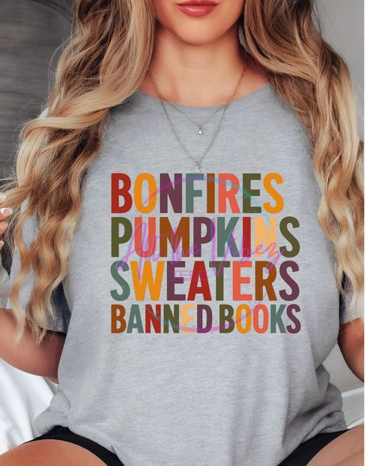 Woman wearing Bonfires, Pumpkins, Sweaters & Banned Books fall graphic tee with colorful autumn lettering celebrating cozy season and the freedom to read.